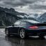 Porsche 997 Carrera 4S bleu foncé sur route de montagne humide, vue de trois-quarts arrière