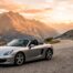 Porsche Boxster de base grise garée sur une route de montagne au coucher du soleil