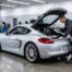 Technicien inspectant un Porsche Cayman gris dans un garage de service, contrôle Porsche Approved