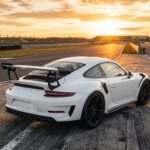 Porsche 997 GT3 RS blanche sur un circuit au coucher du soleil, aileron arrière fixe et jantes noires