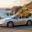 Porsche 911 997 Cabriolet argent, capote ouverte, sur une route côtière